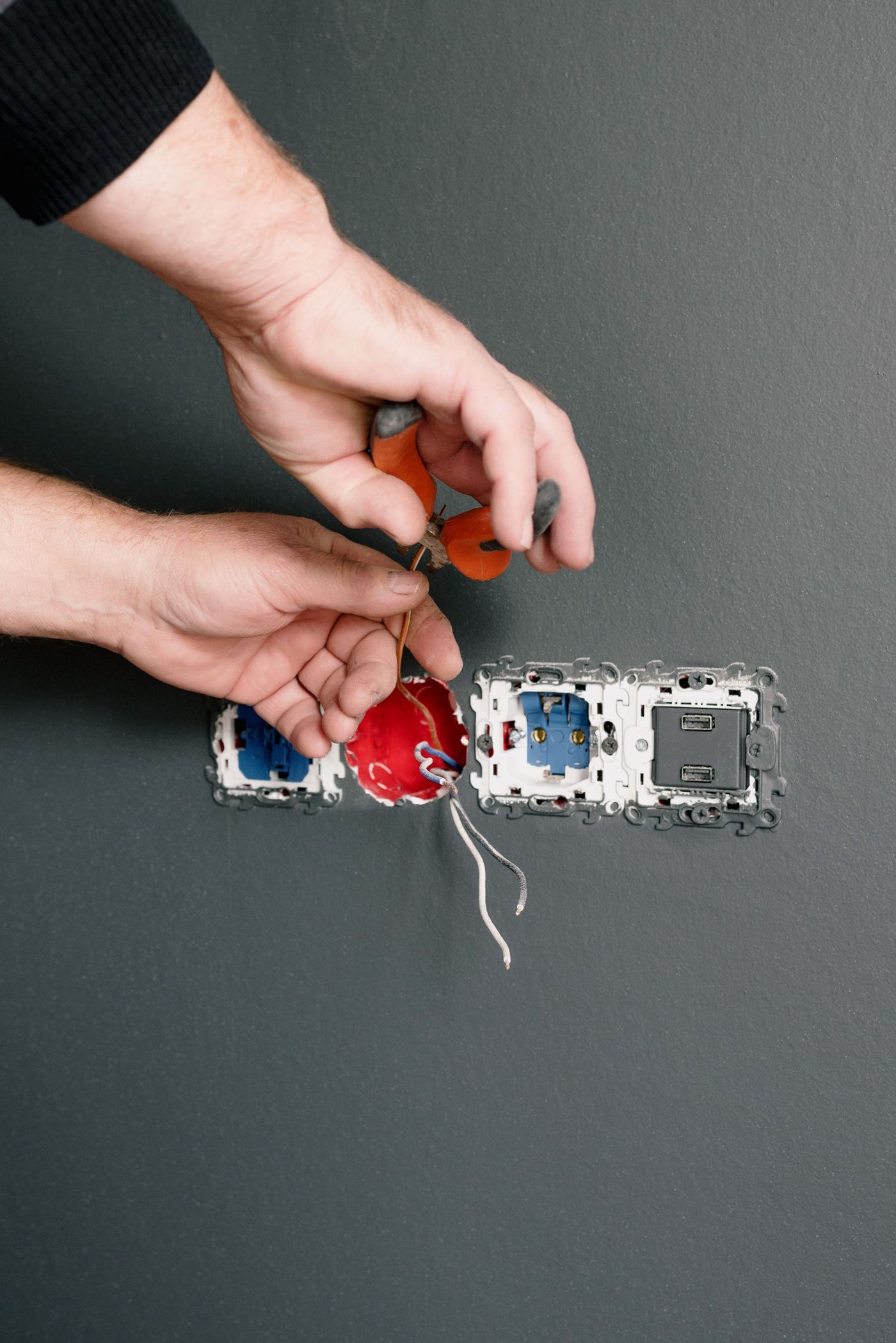 Hands installing a wall outlet with pliers
