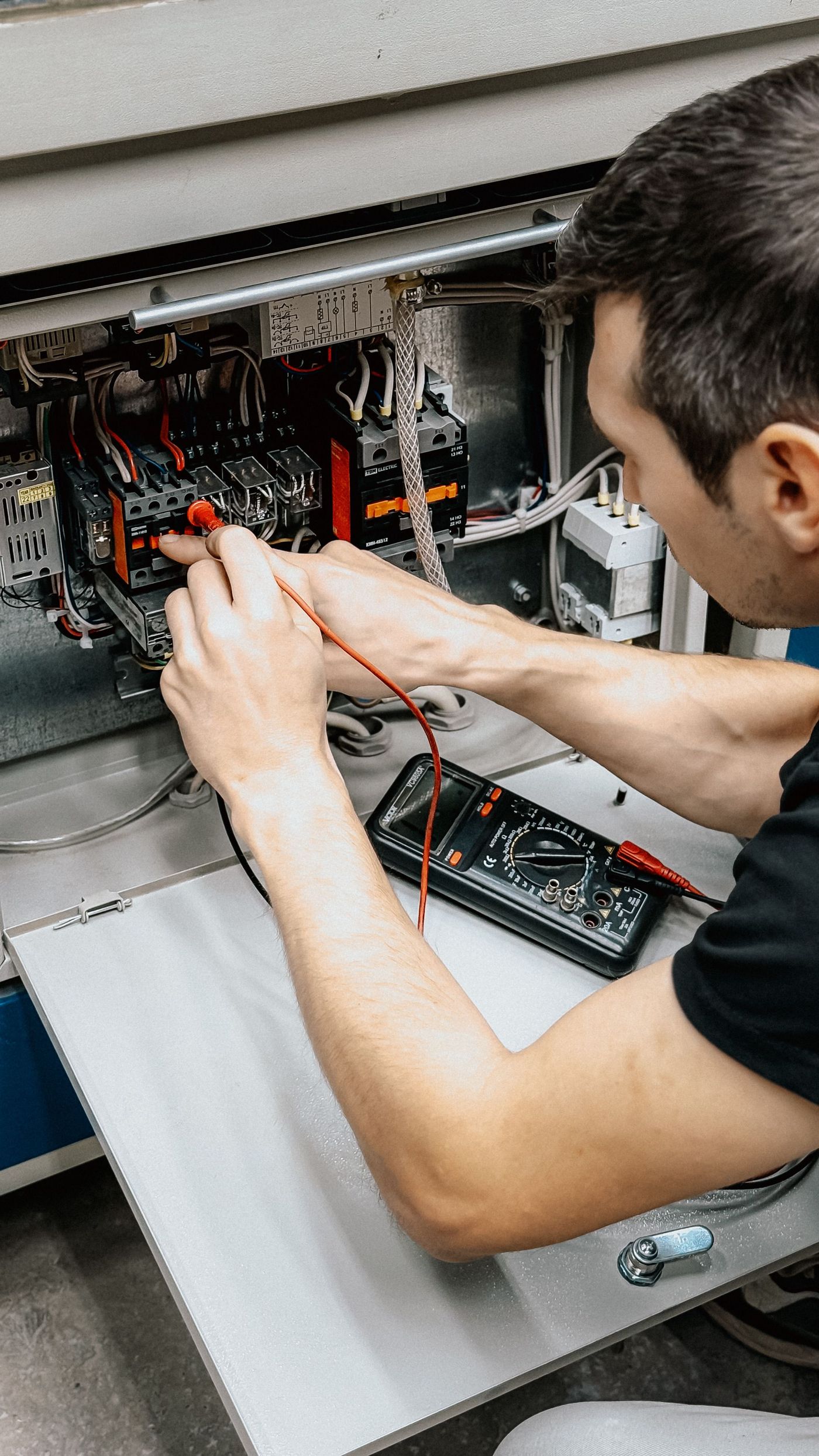 Electrician testing connections inside an open electrical panel with a multimeter