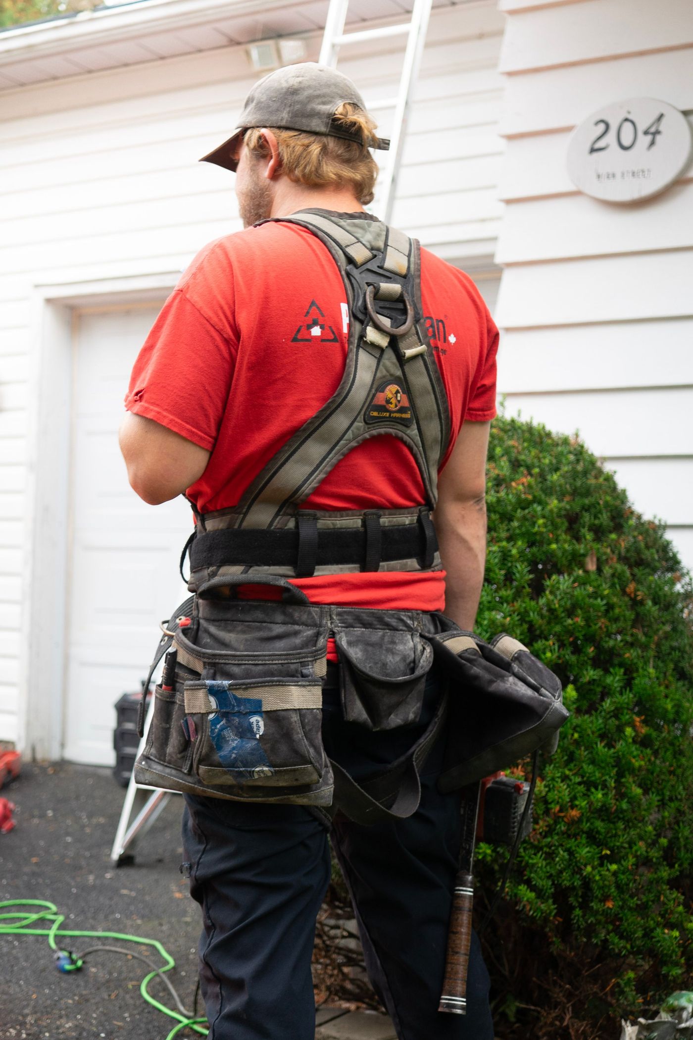 Worker in a harness and tool belt beside a white house, seen from behind
