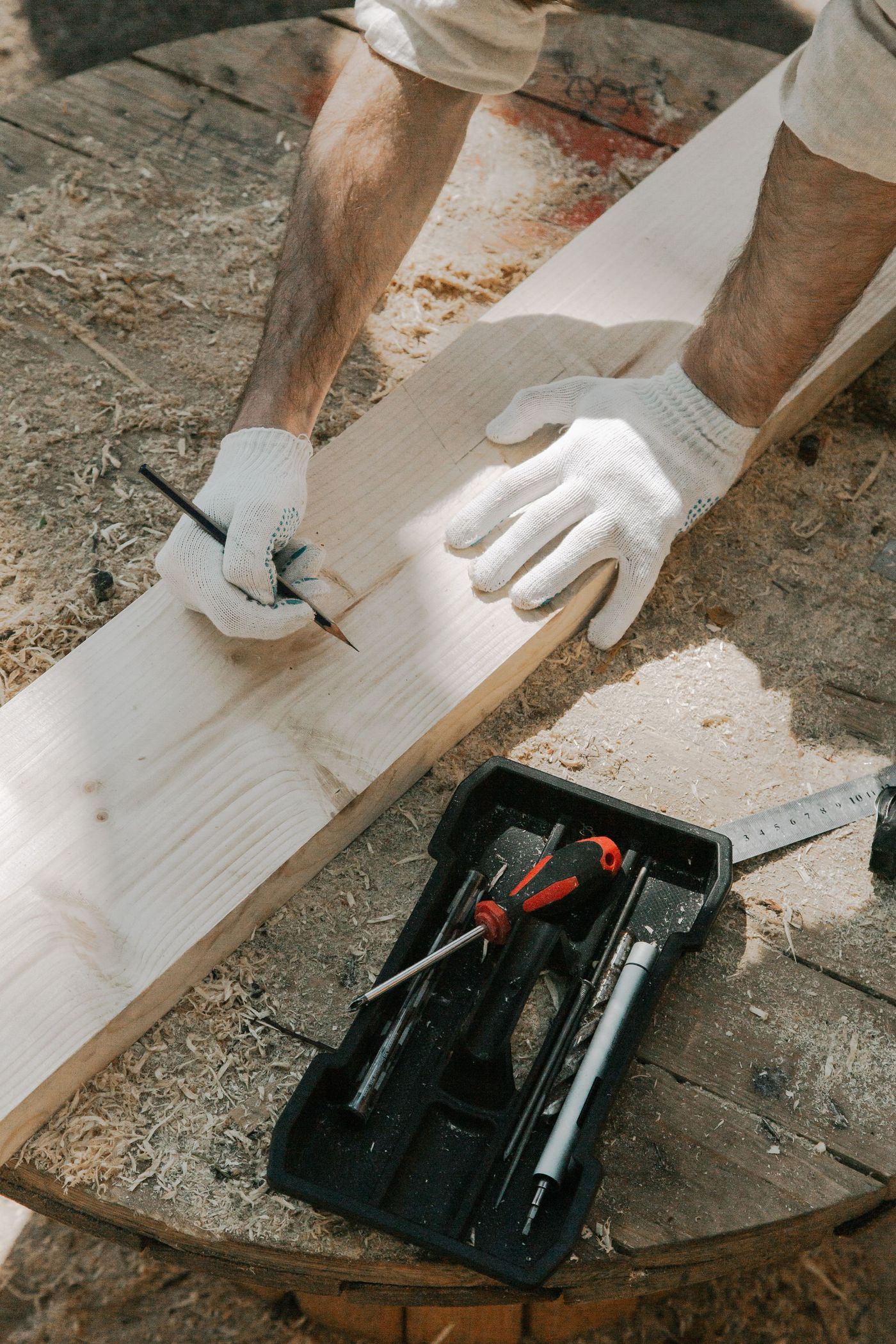 Gloved hands measuring and marking a wood plank with a tape measure and pencil