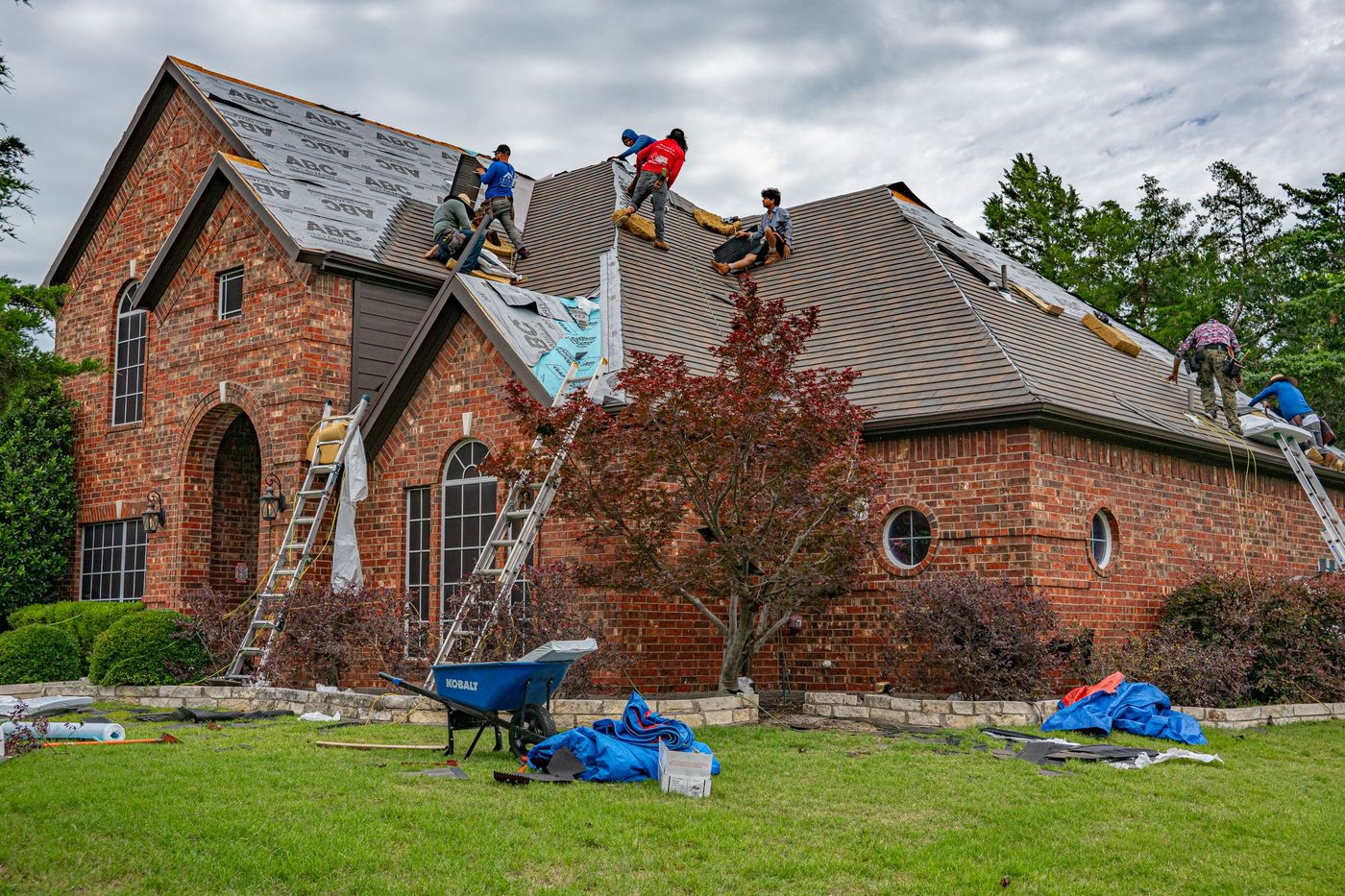 Two roofers handling shingles on the roof of a brick house