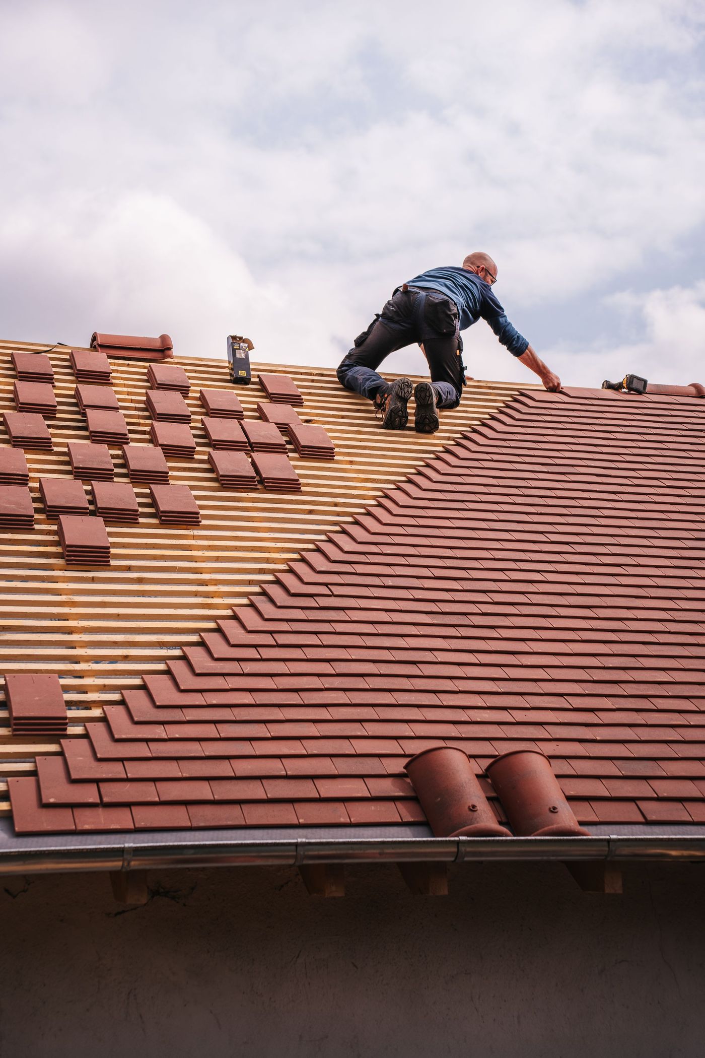Roofer fitting shingles on a new residential roof under cloudy skies