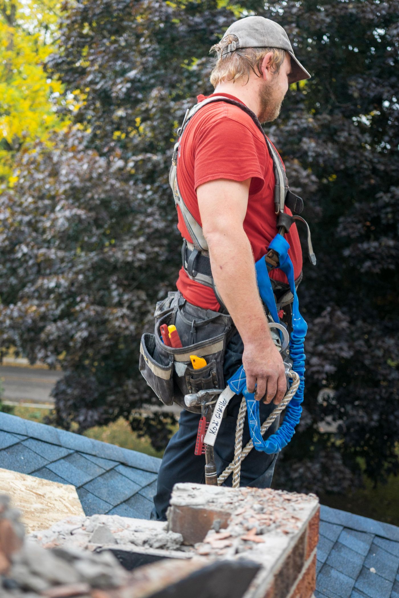 Worker in safety gear on a residential rooftop checking a chimney